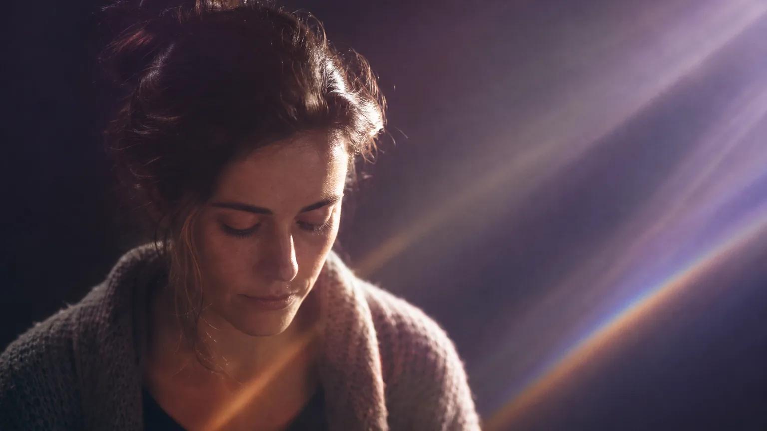 A woman in a knit cardigan looking down softly, calm, in violet light.