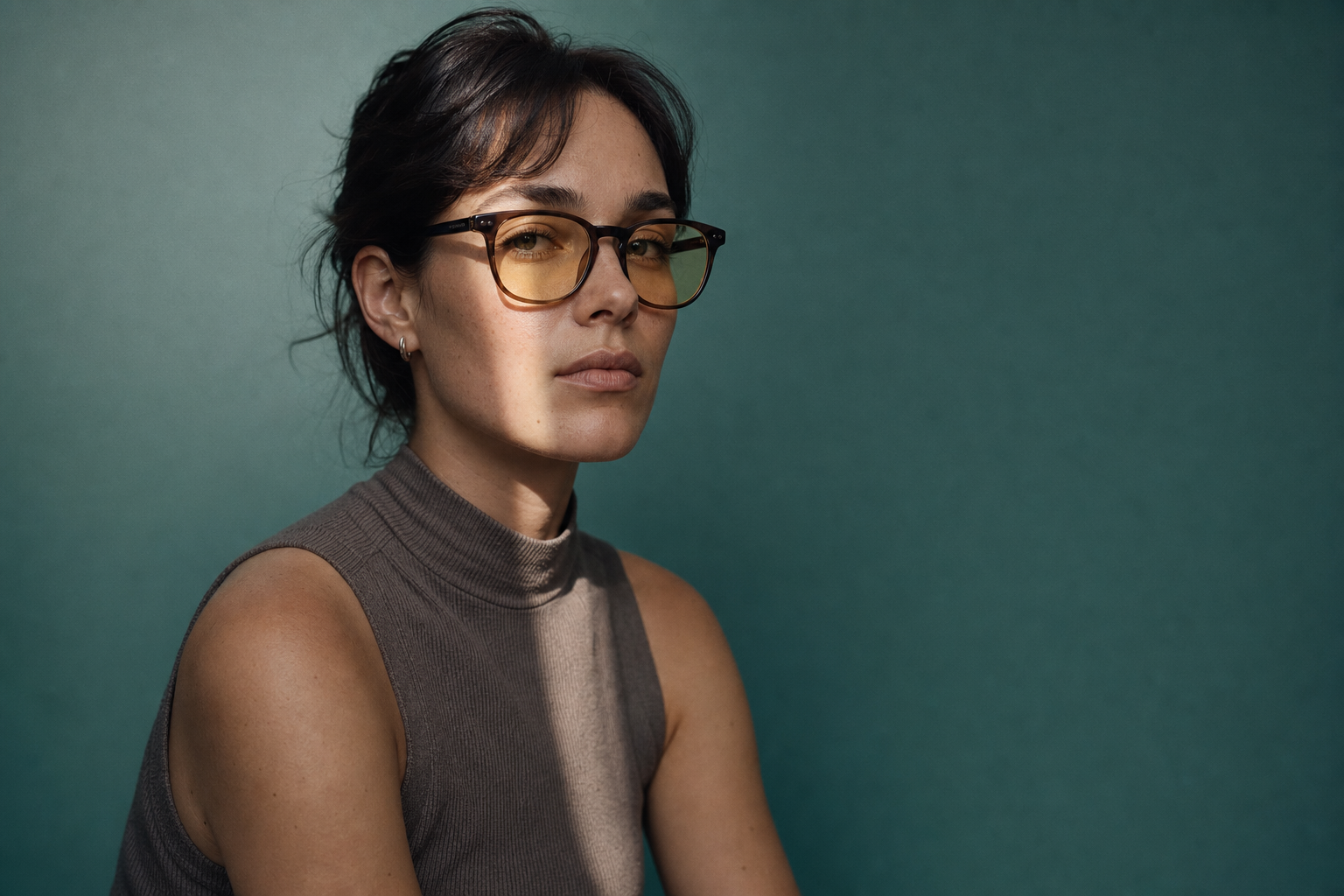 A woman in glasses looking towards the camera against a deep green backdrop