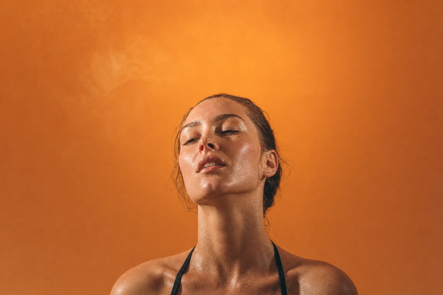 A woman with her eyes closed and head tilted back against a warm orange backdrop